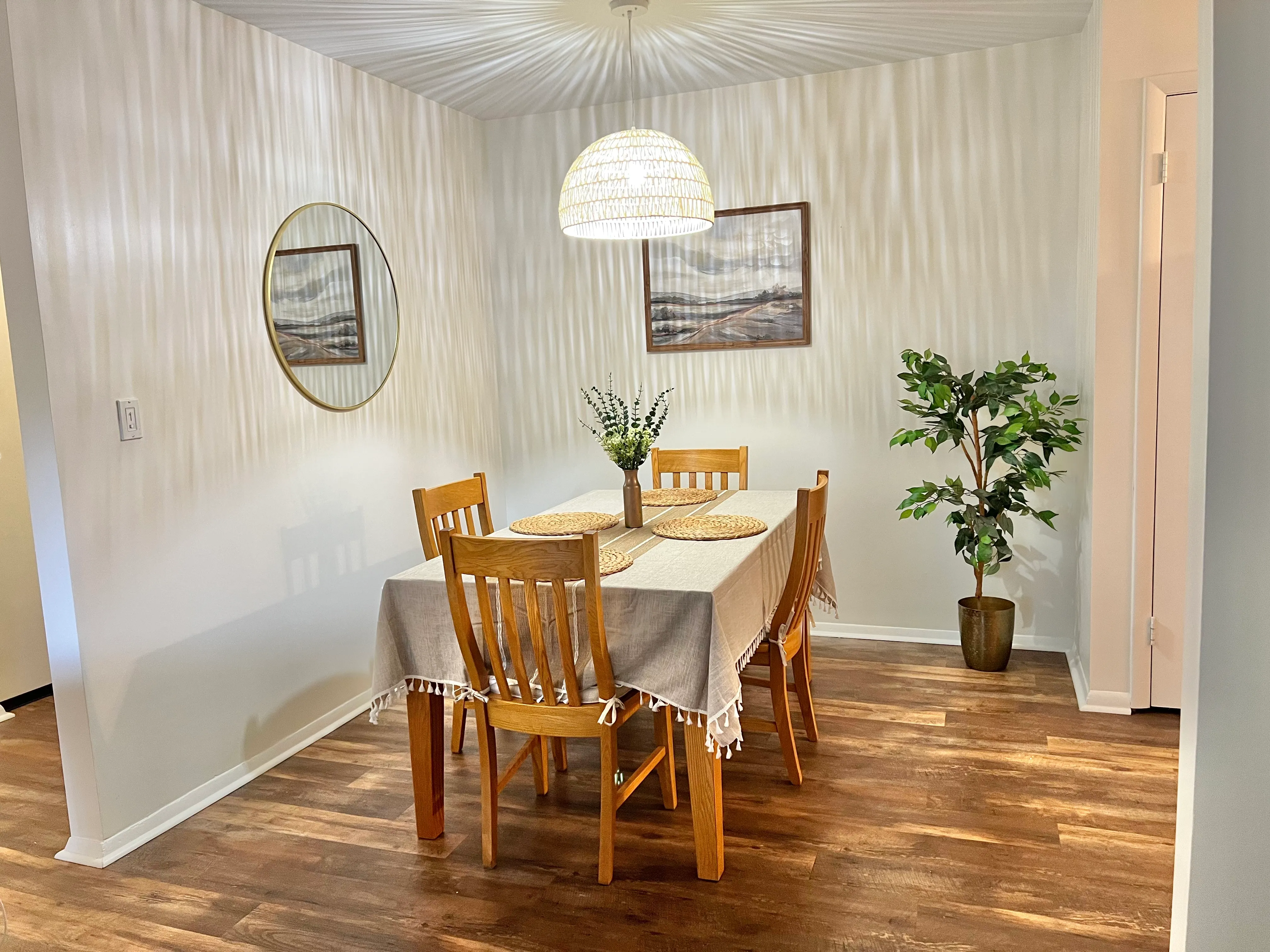 Dining nook with a wood table, woven placemats, and framed landscape art